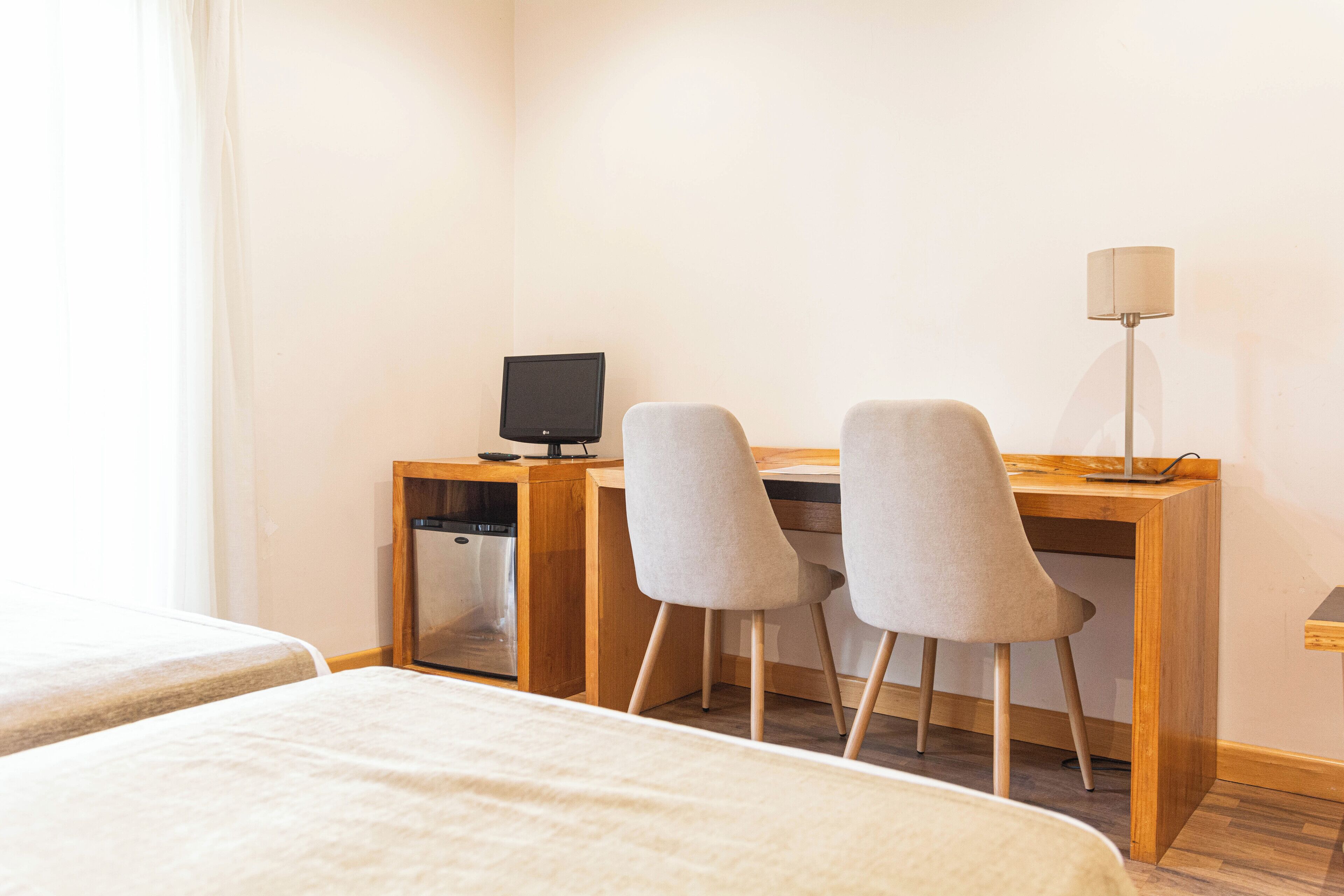 Une chambre d’hôtel avec un bureau en bois, deux chaises grises, une télévision, une lampe et une petite machine à laver.