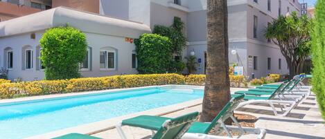 A pool area with lounge chairs, a palm tree, and a building with balconies.