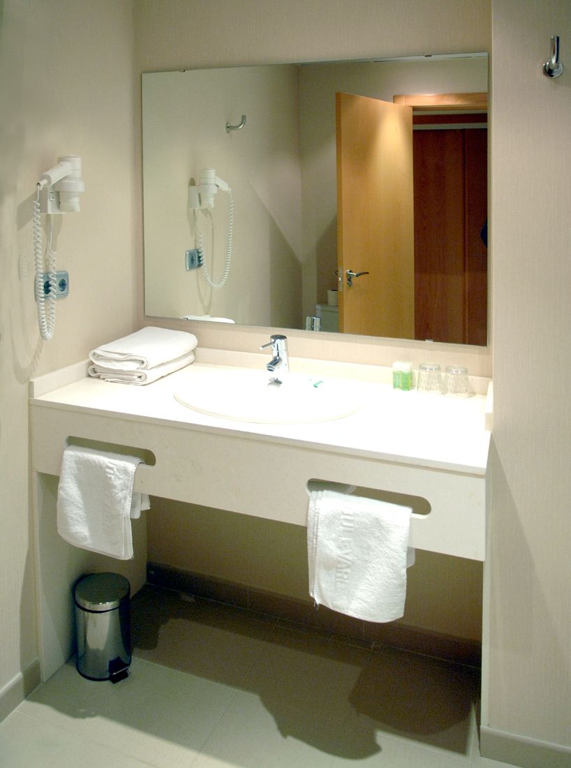 Une salle de bain d’hôtel équipée d’un double lavabo, d’un miroir, d’un porte-serviettes et d’une poubelle.