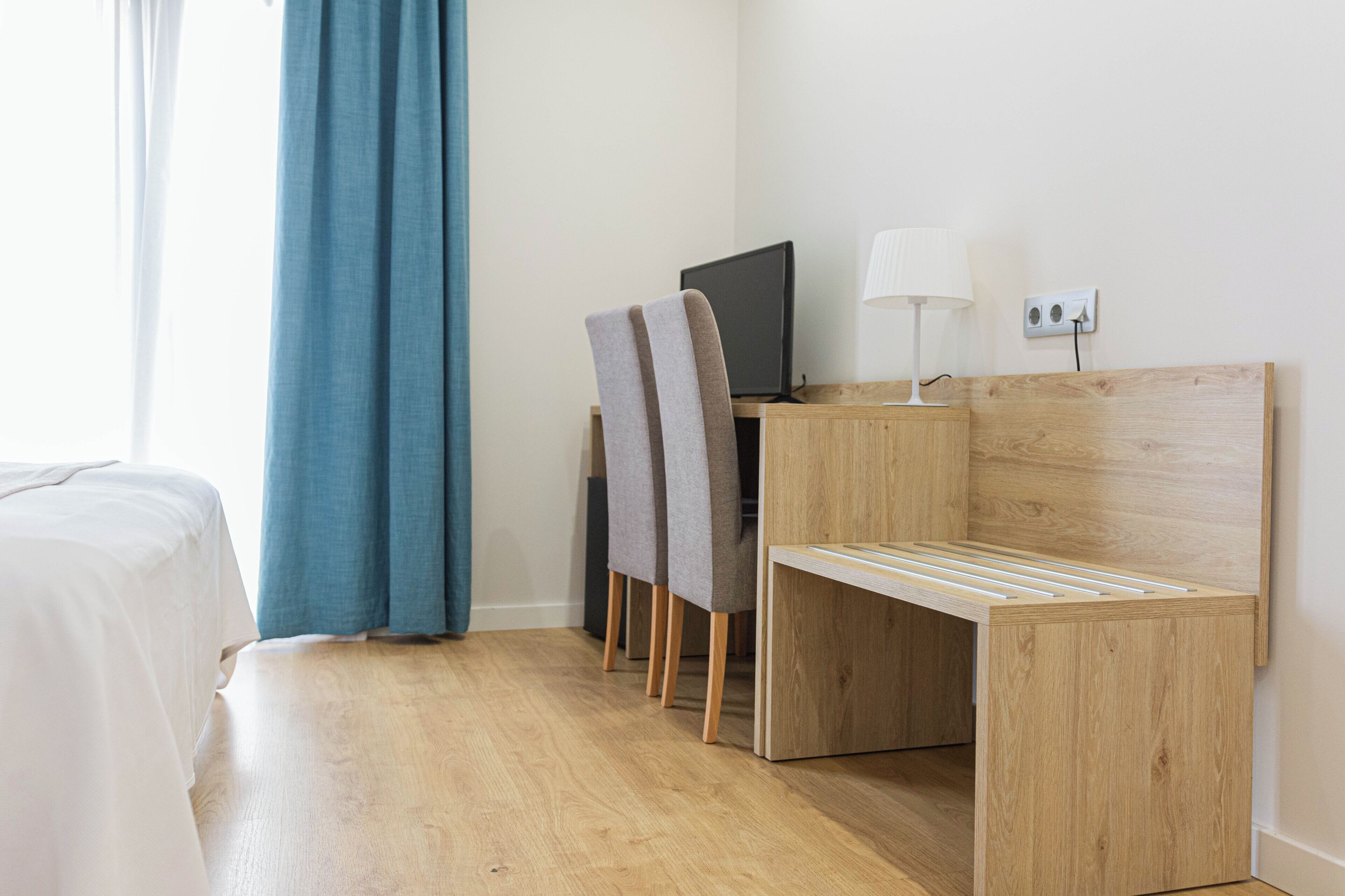 Una habitación de hotel con cama, un escritorio con computadora y lámpara, y una silla.