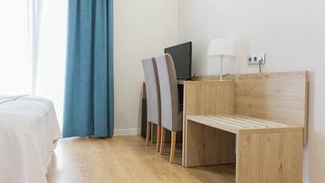 Una habitación de hotel con cama, un escritorio con computadora y lámpara, y una silla.
