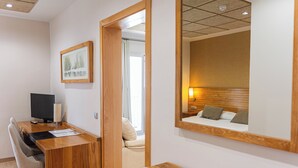 A hotel room with a wooden desk, a chair, a bed with pillows, a bedside table, a mirror, and a framed picture on the wall. - Hotel Bulevard (Benicassim)