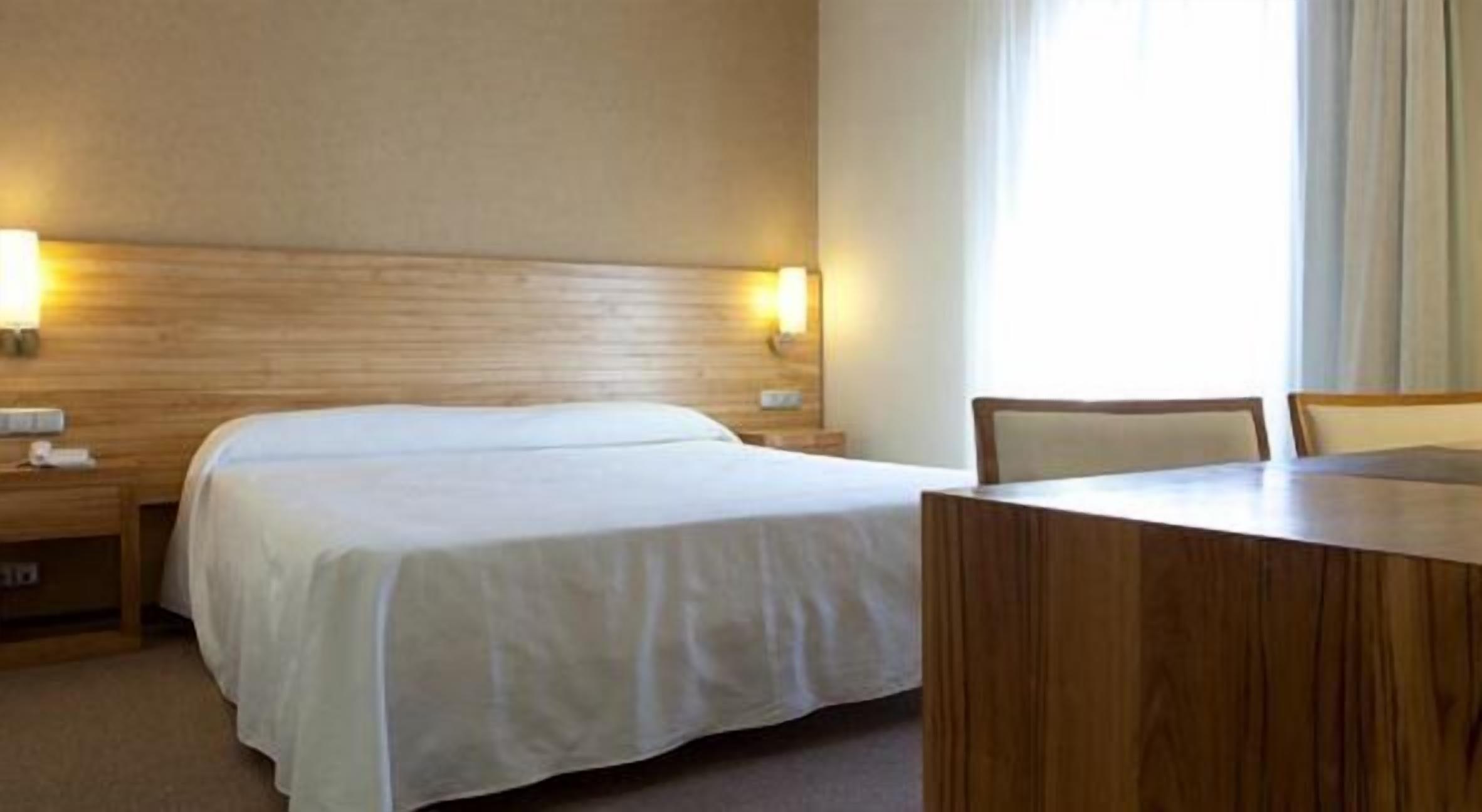 Habitación de hotel con una cama grande, cabecera de madera, mesita de noche, escritorio y una silla.