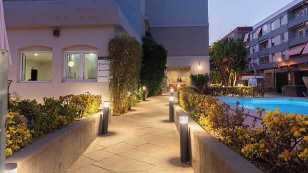 A pathway leading to a pool area with a building on one side and a reception desk visible in the background. - Hotel Bulevard (Benicassim)