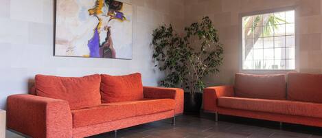 A modern living room with two orange sofas, a large abstract painting, a potted plant, and a window with natural light.