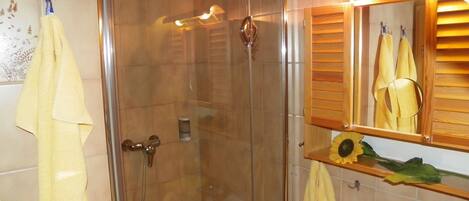 A bathroom with a glass-enclosed shower, a wooden vanity with a mirror, and a yellow towel hanging on the wall.