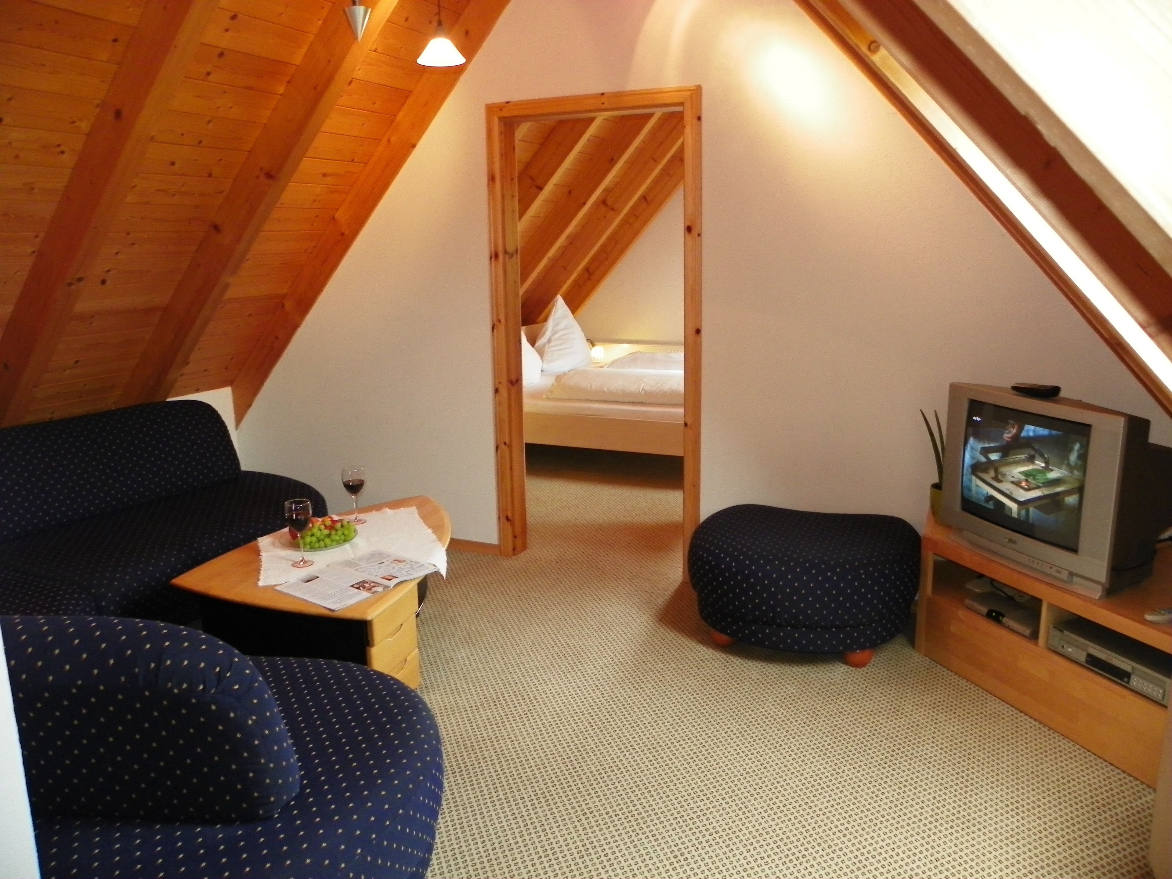 A cozy attic bedroom with a bed, a TV, and a seating area with a table.