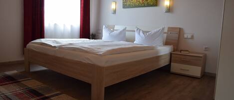 A modern hotel room with a wooden bed, a plaid area rug, a nightstand, a wall-mounted lamp, and a painting.