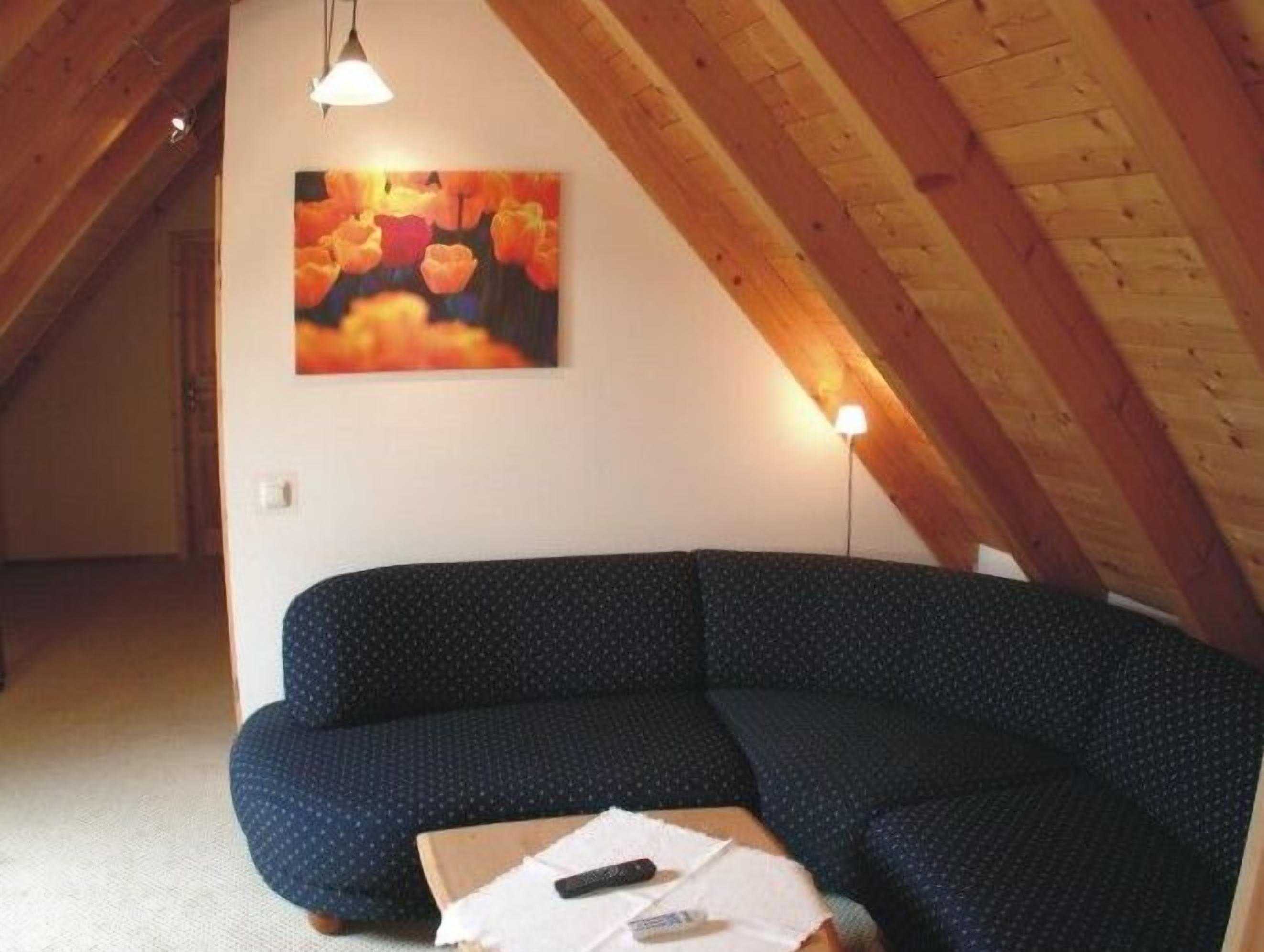 Un cuarto ático acogedor con un sofá azul oscuro, un cuadro de flores y un techo de madera.