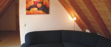Un cuarto ático acogedor con un sofá azul oscuro, un cuadro de flores y un techo de madera.