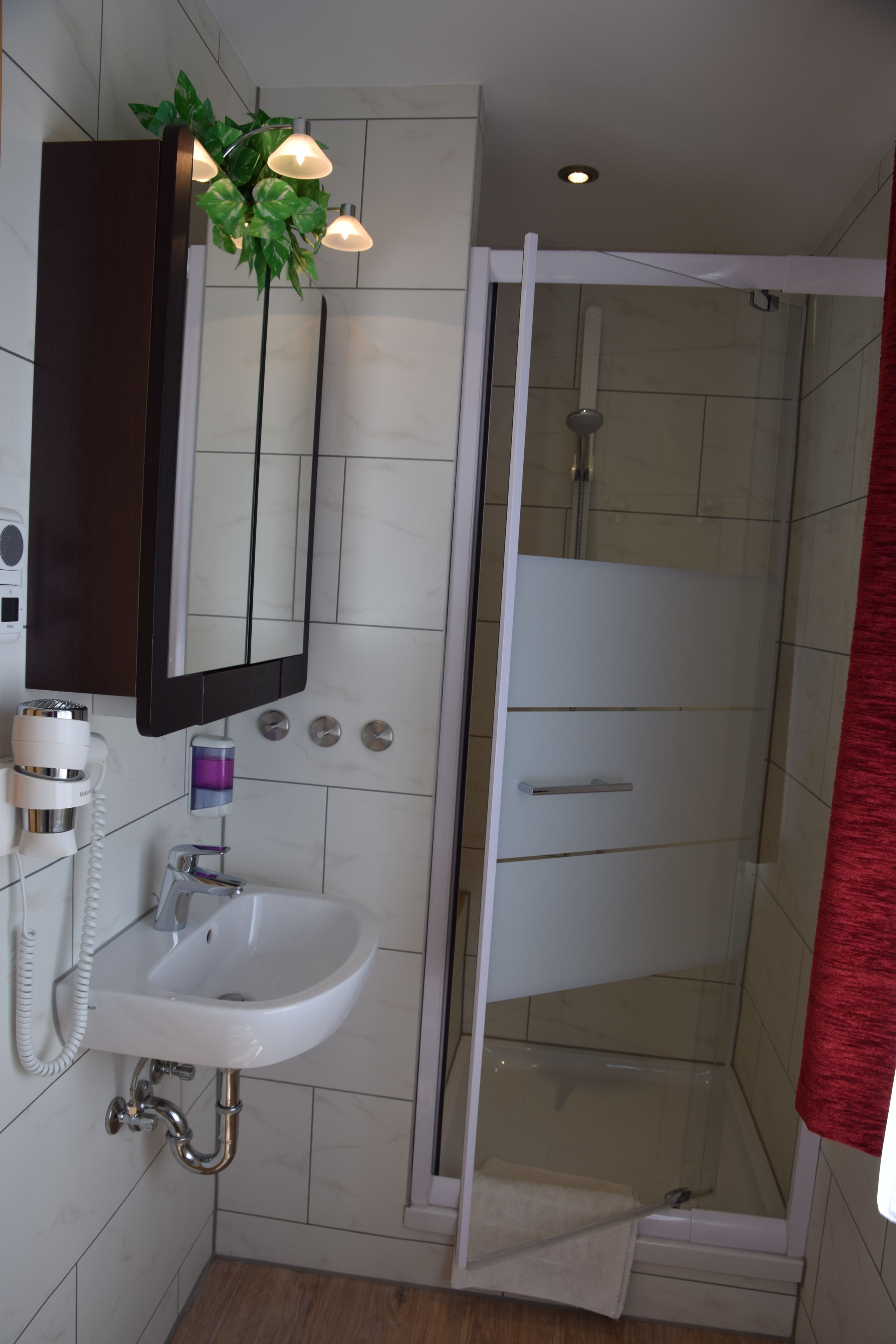 Un baño con lavamanos blanco, un espejo, cabina de ducha y una toalla roja.