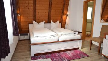 A bedroom with a wooden ceiling, a bed with white bedding, a chair, and a small cabinet.
