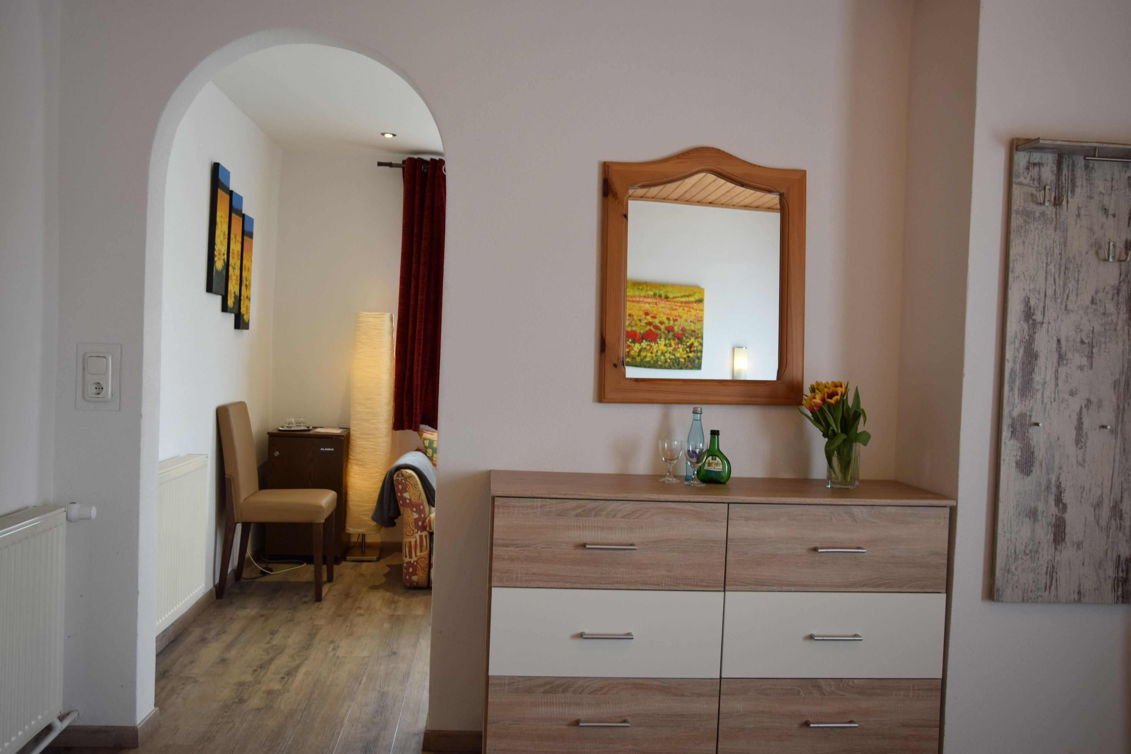 A room with a wooden cabinet, a mirror, and a vase with flowers.