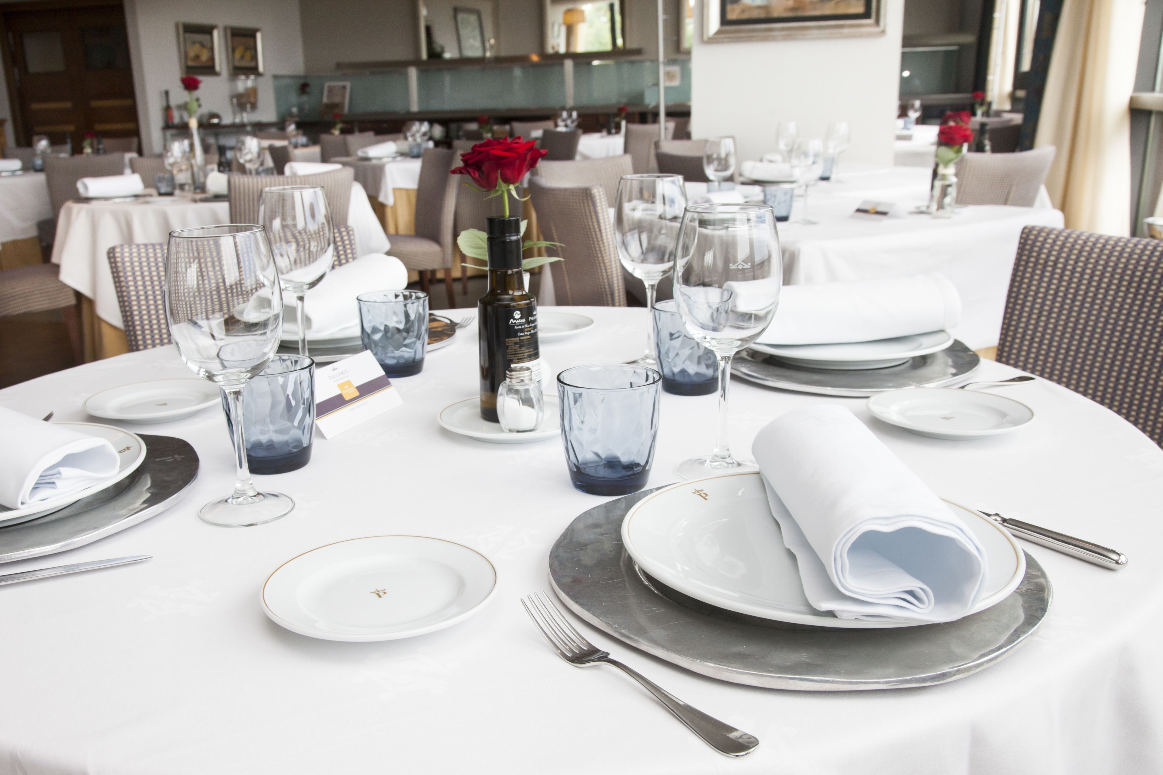 A dining table set with plates, glasses, and a bottle of wine, with a rose in a vase.