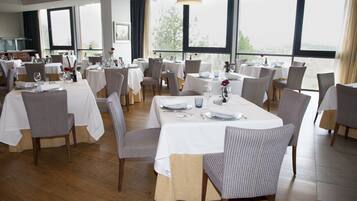 A restaurant with multiple tables set for dining, large windows offering a view, and a clean, modern interior.