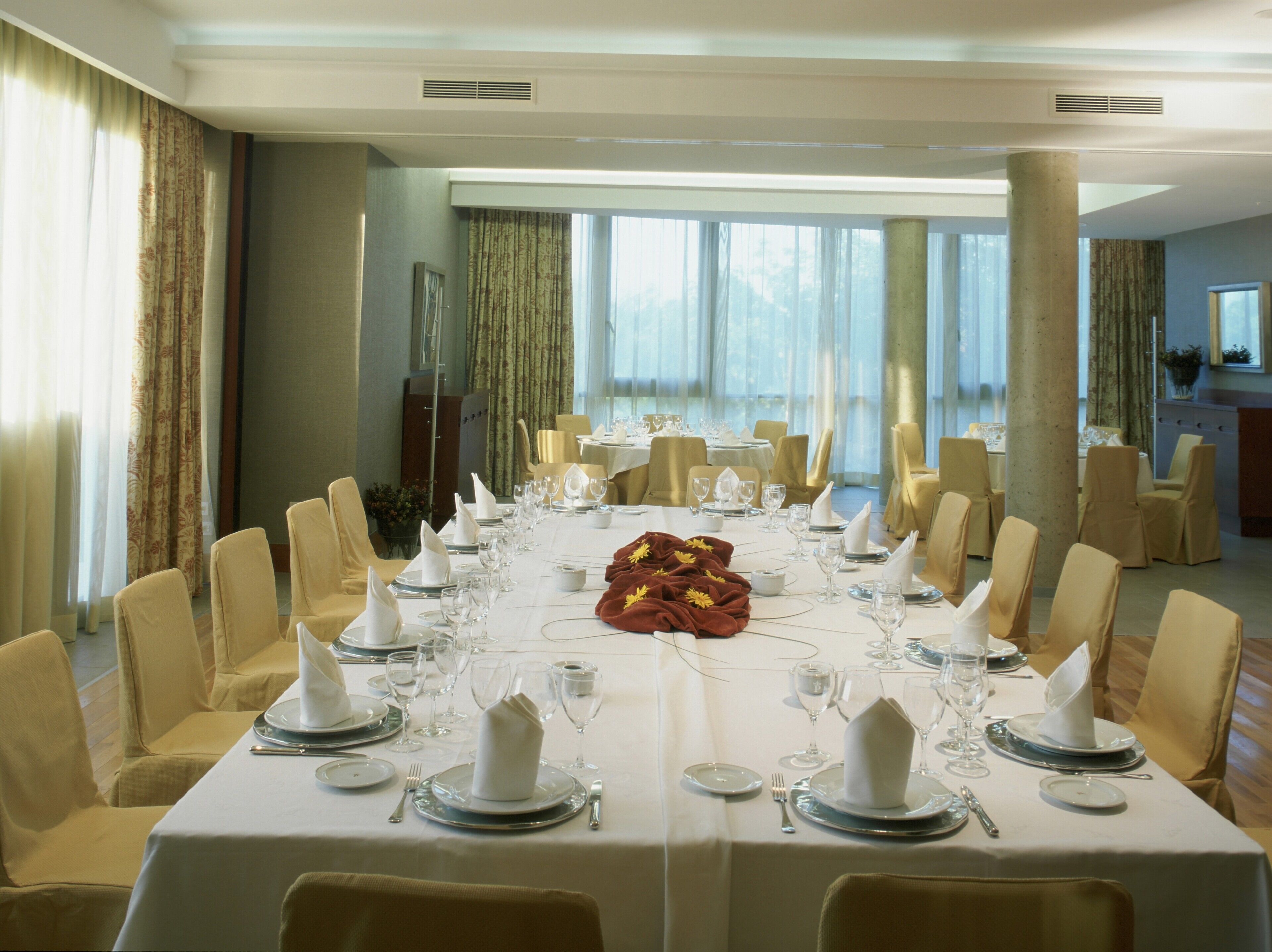 A large, elegantly set dining room with multiple tables, each equipped with fine china, glassware, and comfortable seating.