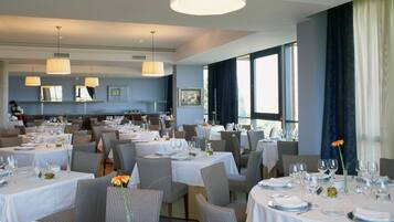 Een restaurant met meerdere eettafels, stoelen en hangende lampen.