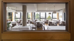 Un restaurante con varias mesas y sillas, ventanas amplias y lámparas colgantes.