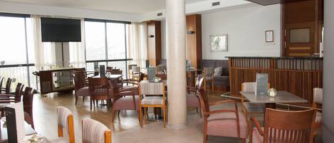 A spacious dining area with multiple tables and chairs, a large pillar, and a television screen on the wall.