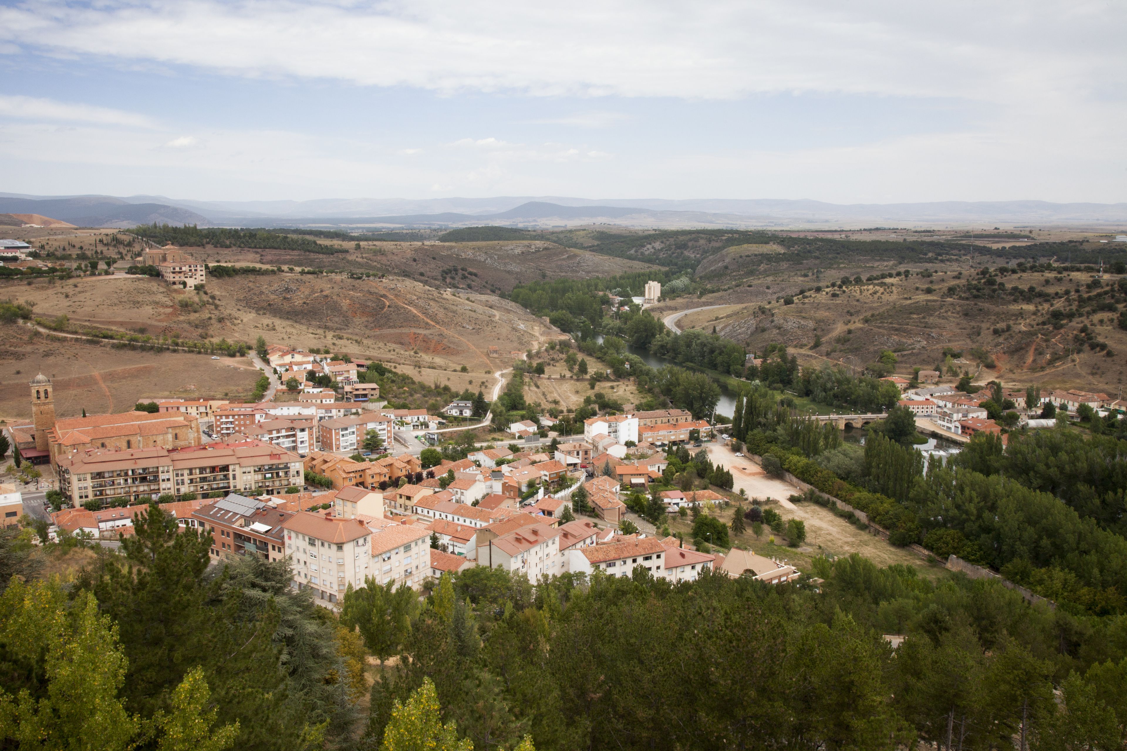 Un pueblo con una mezcla de edificios residenciales y comerciales, una iglesia destacada y un río que atraviesa el valle.
