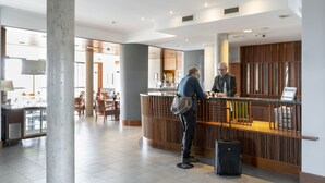 Zona de recepción de hotel con un mostrador de madera, un pilar grande y un área de estar al fondo.