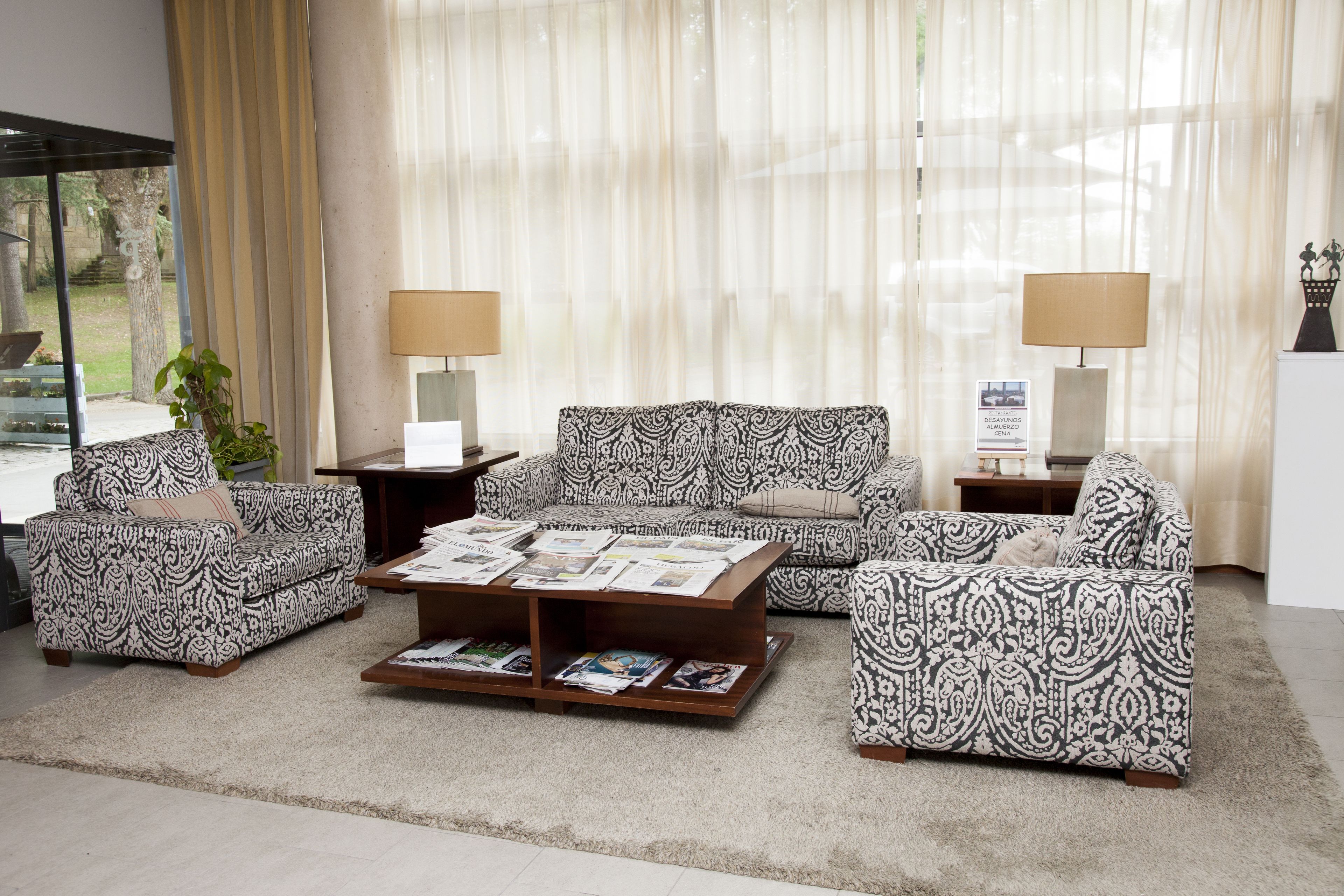 A living room with patterned sofas, a coffee table with magazines, and two lamps.