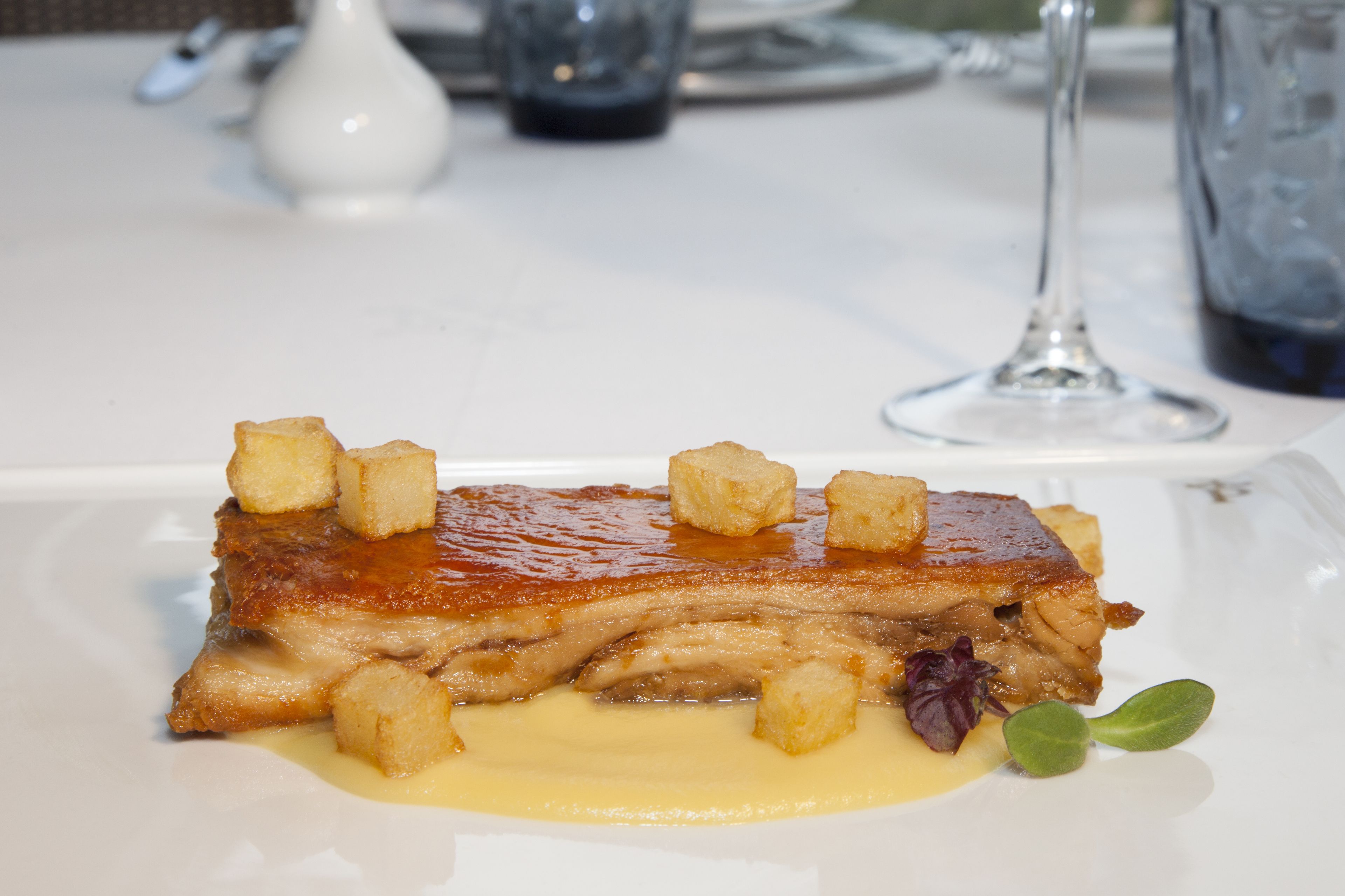 En anretning med glasérstegt sværs ribben, brødtern og sauce, pyntet med et blad, serveret på en hvid tallerken.