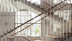 Interior de varios niveles con una escalera, barandillas de metal y grandes ventanales que dejan entrar luz natural.