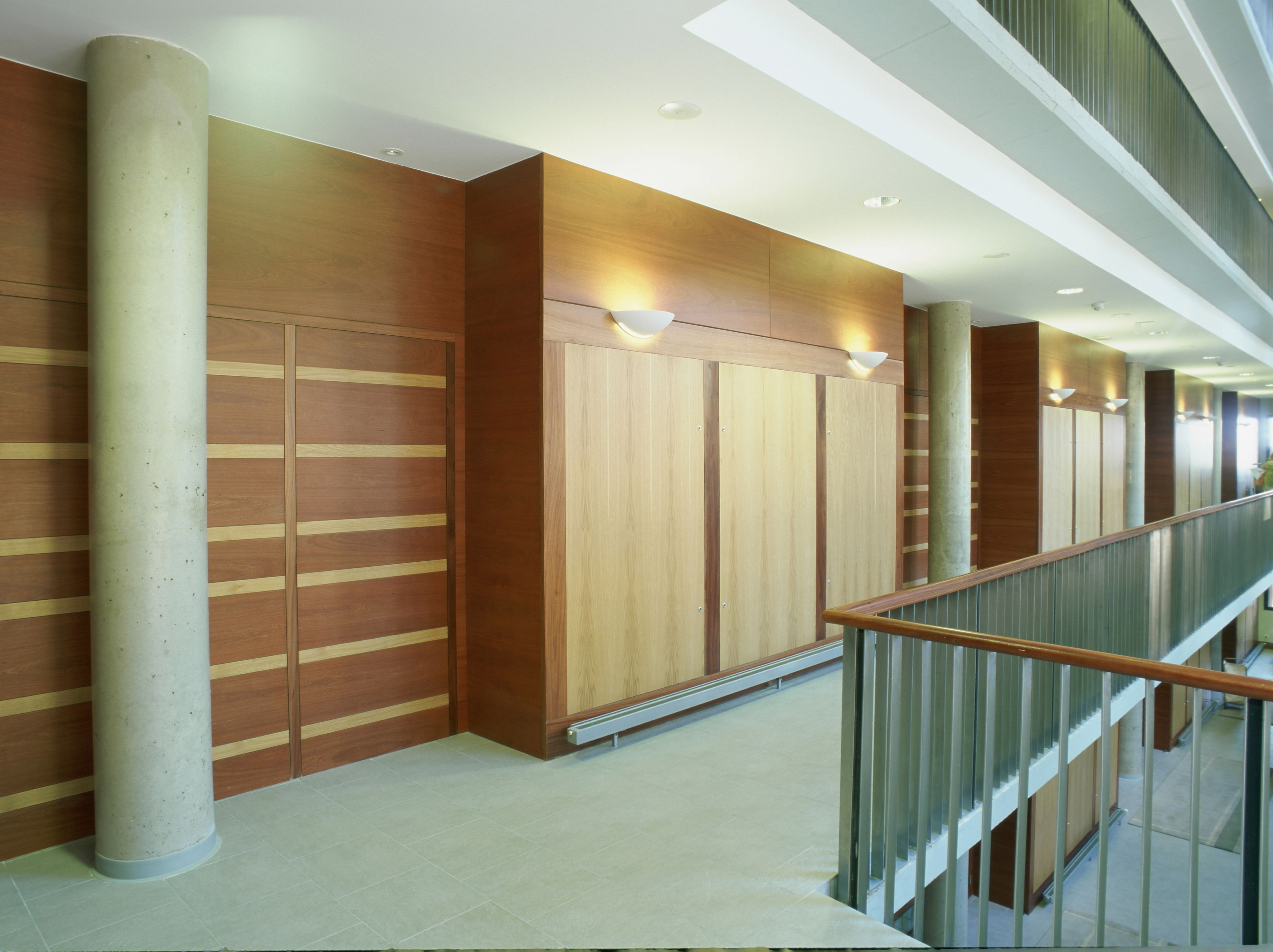 A modern interior with wooden panel walls, a concrete column, and a glass railing.