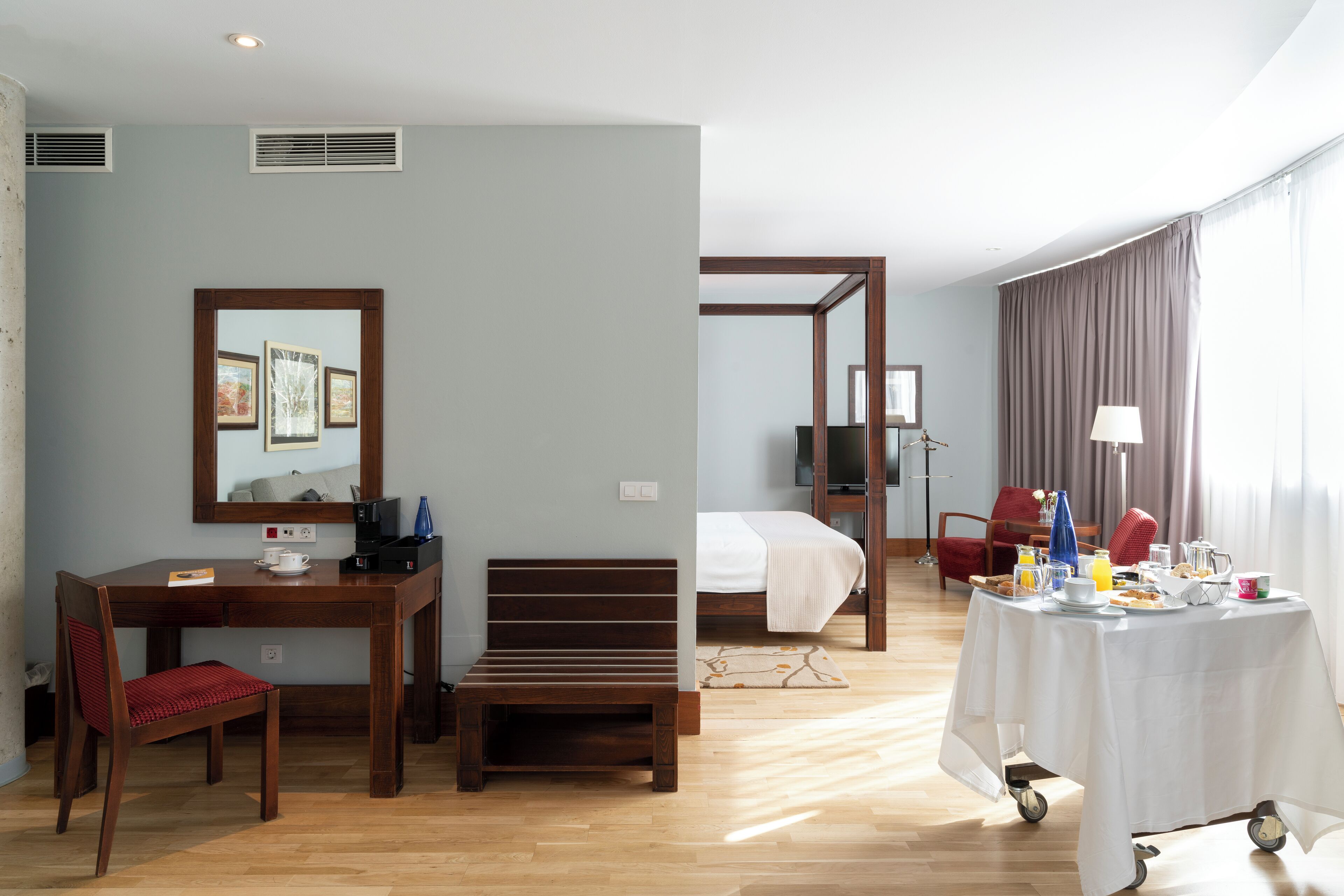 Habitación de hotel con escritorio de madera, una silla, una cama y una mesa de desayuno servida.