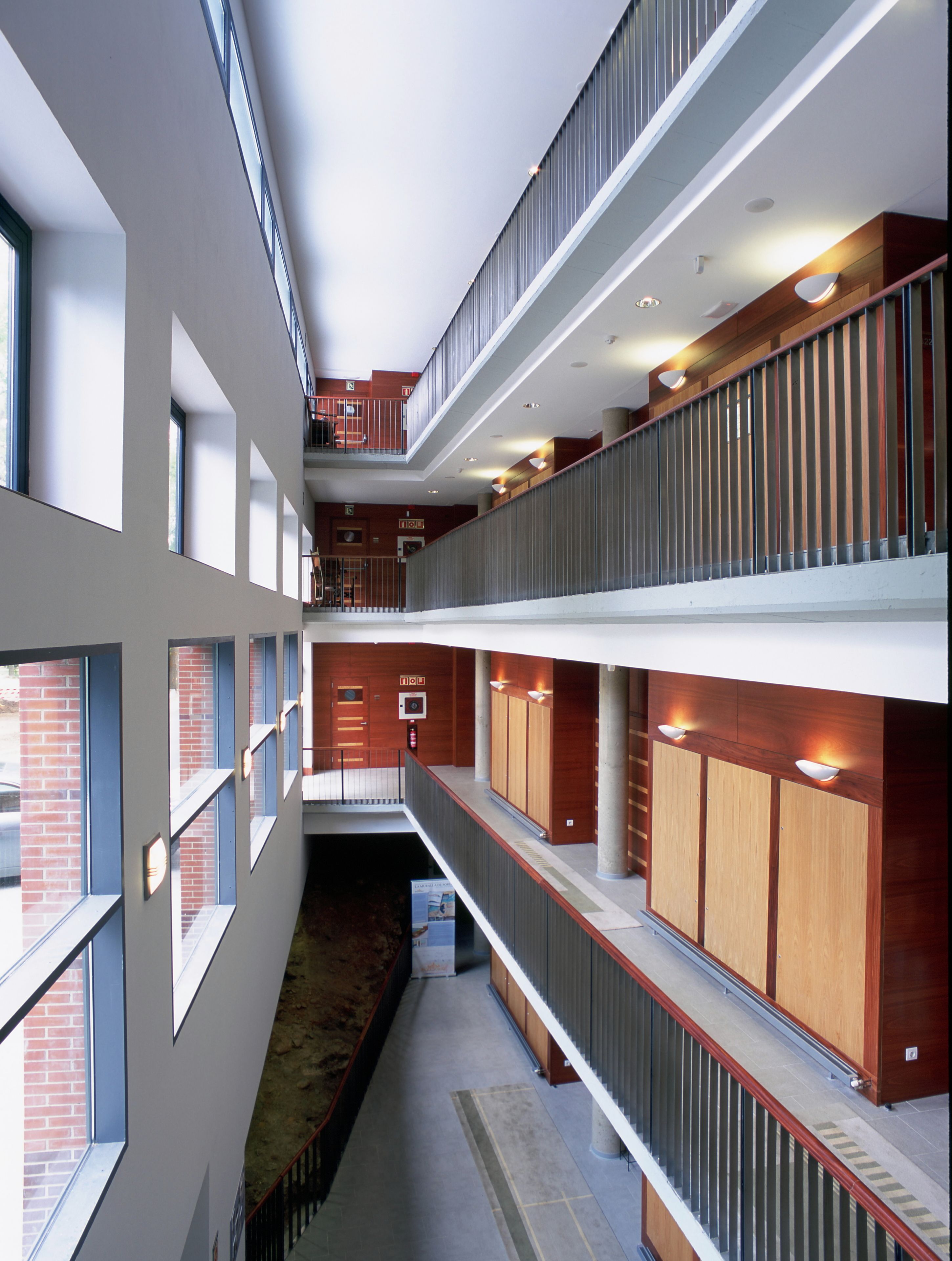 Un interior de varios niveles con una escalera central, paneles de madera y un corredor con vistas.