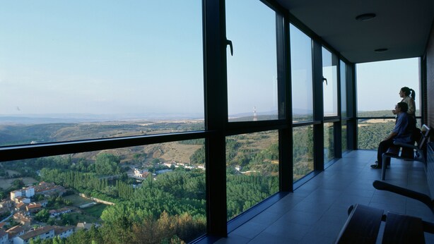 Amplia habitación con grandes ventanales que ofrecen una vista panorámica de un paisaje con edificios y vegetación.