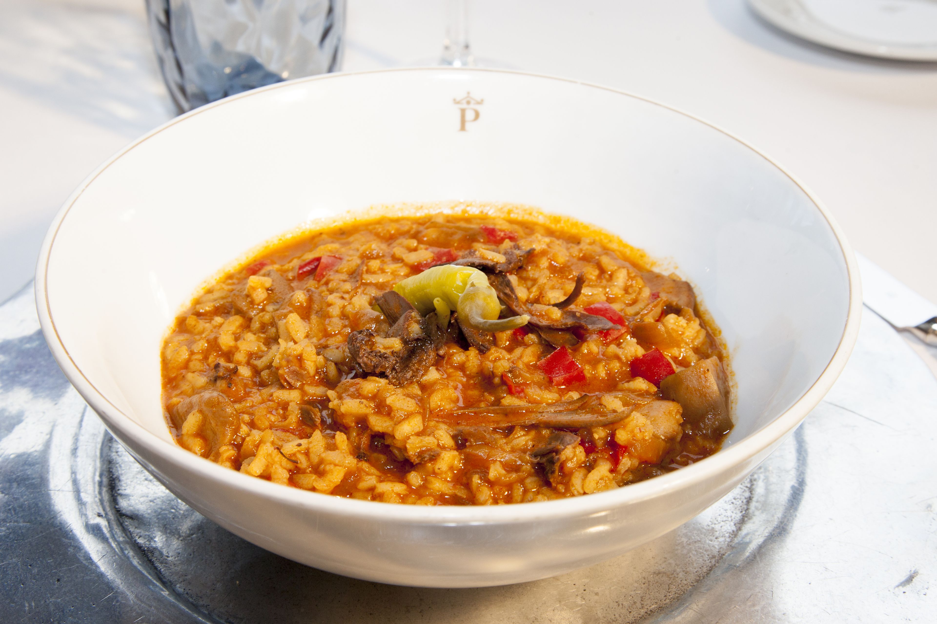 A bowl of rice dish with vegetables and meat, served on a white plate with a gold rim.