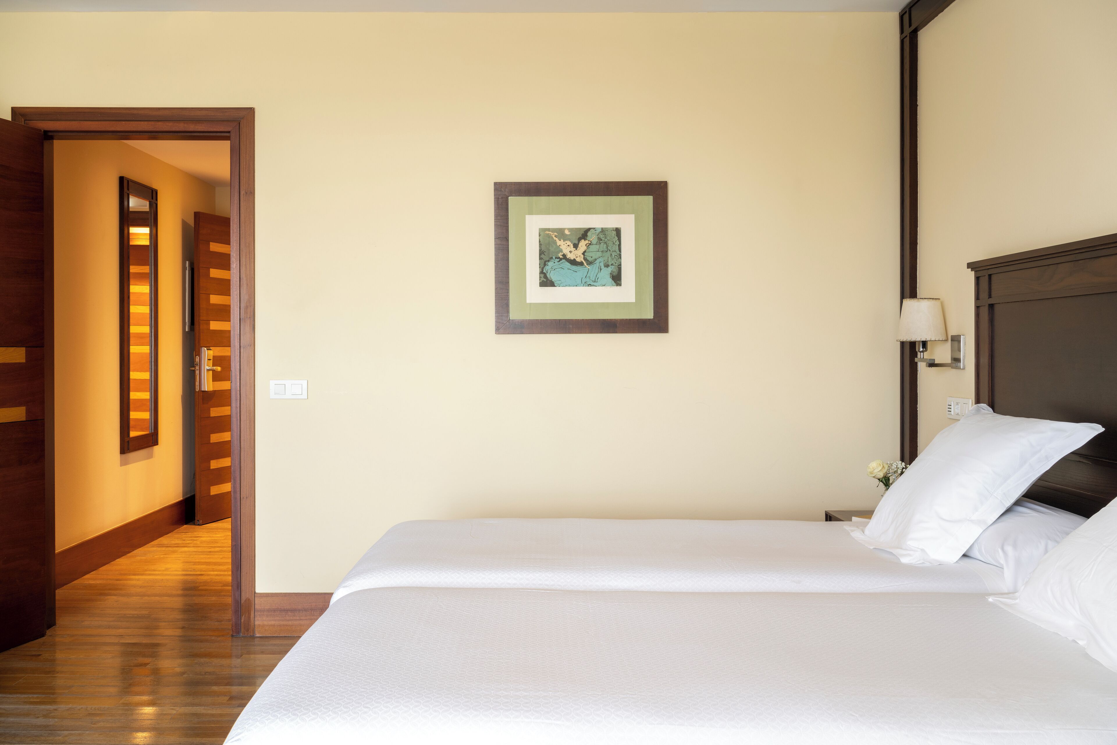 Una habitación de hotel con una cama grande, una obra de arte enmarcada en la pared, una mesita de noche con una lámpara y piso de madera.
