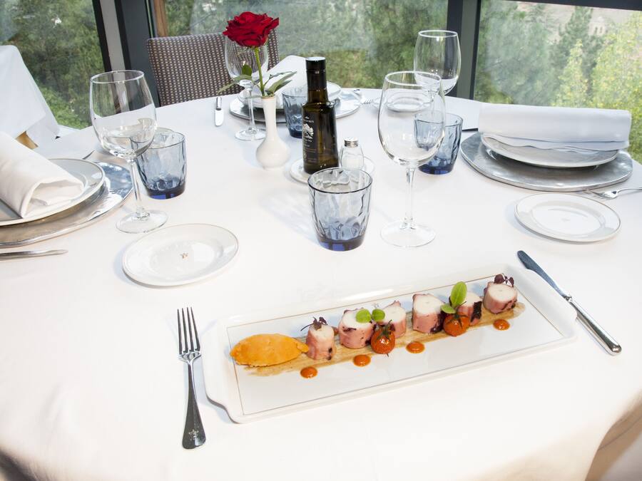 Una mesa lista para comer, con mantel blanco, una botella de vino y un plato de comida.
