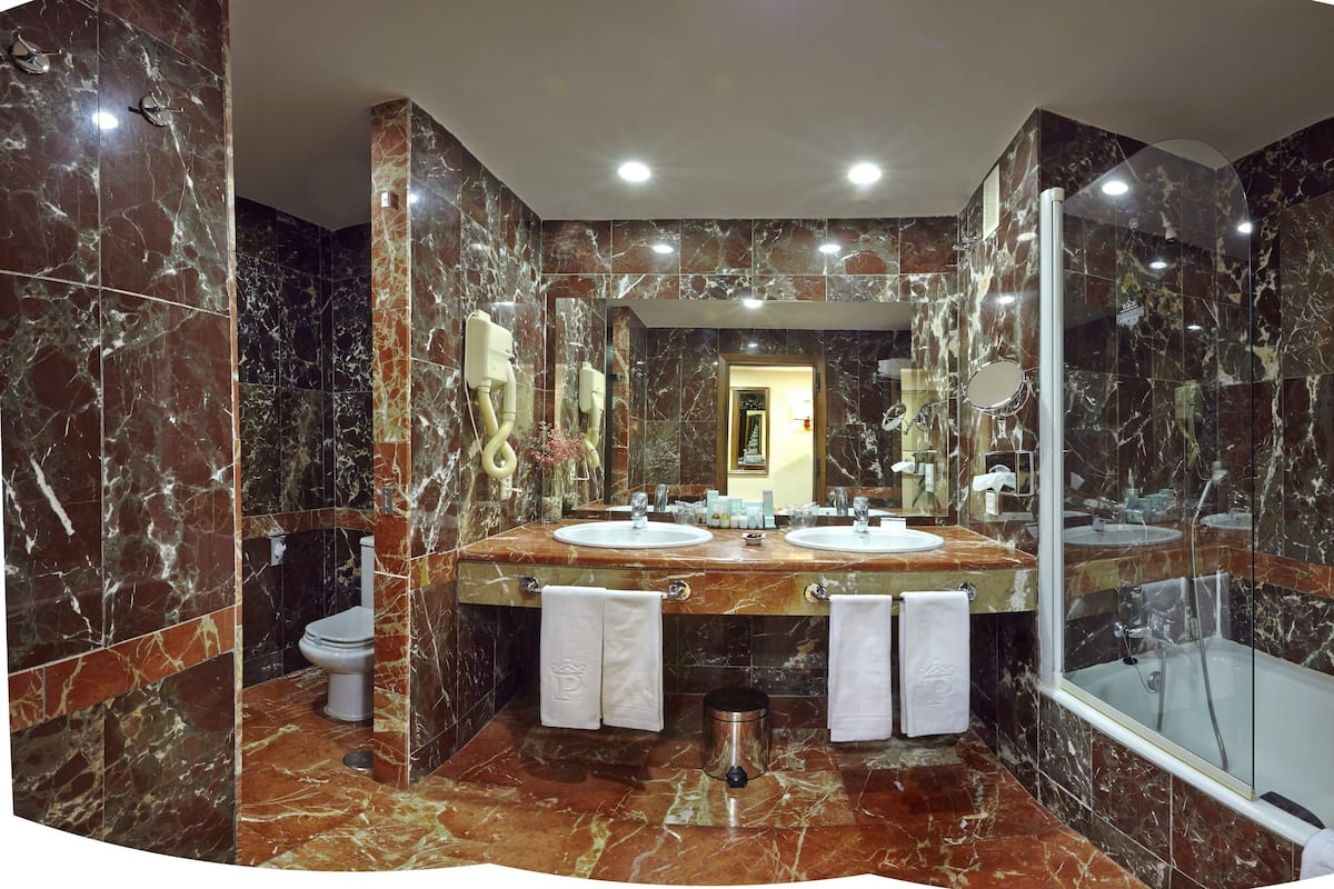 A luxurious bathroom with marble walls, two sinks, a toilet, a mirror, and a bathtub.
