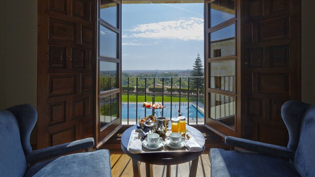 Un balcón con una mesa dispuesta para el desayuno, con vista a una piscina y un paisaje verde.