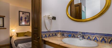 Een hotelbadkamer met een wit wastafelmeubel, een spiegel met gouden lijst en een blauw-geel betegelde achterwand.