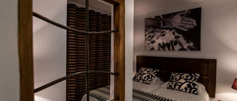 A bedroom with a bed, patterned bedding, a headboard, a nightstand, a lamp, and a wall-mounted artwork.