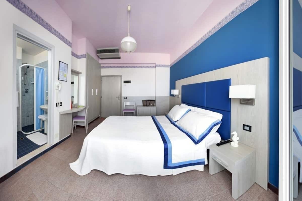 Ein Schlafzimmer mit einem großen Bett, Nachttischen, einem Schreibtisch und einer Dusche.