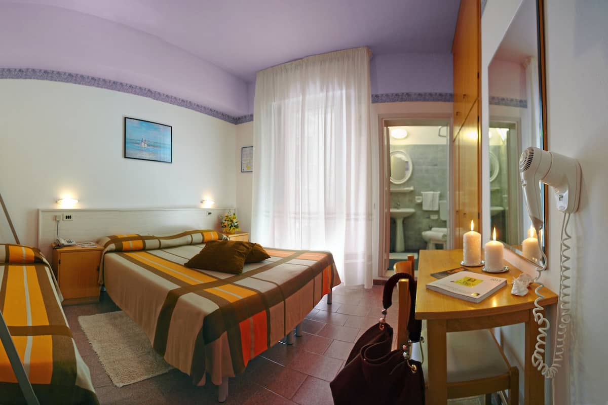 Ein Hotelzimmer mit zwei Betten, einem Schreibtisch mit Telefon und einem Spiegel, und einem durch eine offene Tür einsehbaren Badezimmer.