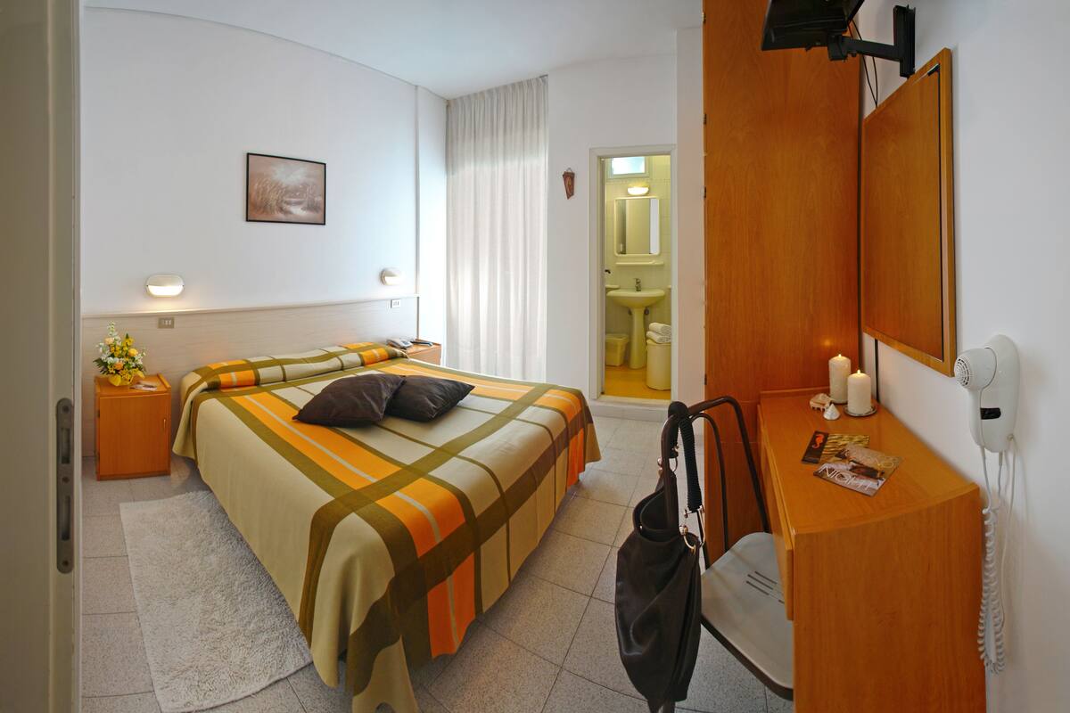 Ein Hotelzimmer mit Bett, Schreibtisch, Spiegel und einem durchgegangenen Tür sichtbaren Badezimmer.