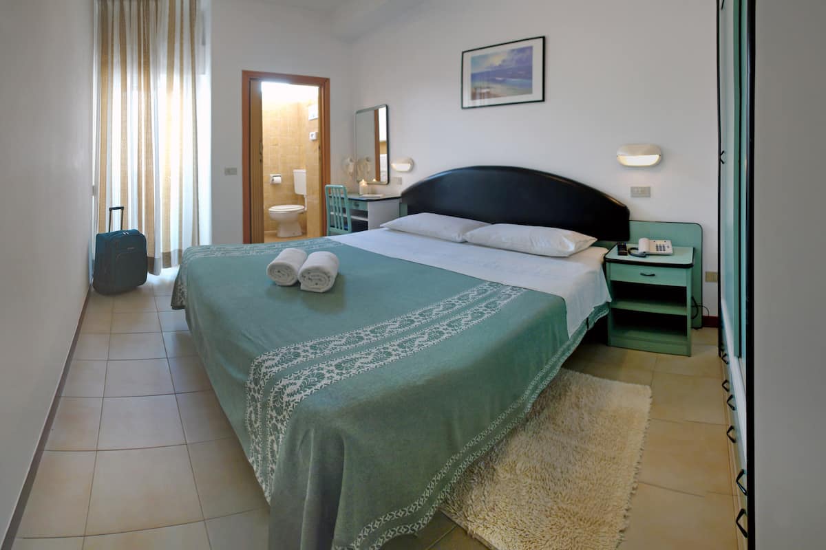 Ein Hotelzimmer mit Bett, Nachttisch, Stuhl, Koffer und einem durchgegangenen Tür sichtbaren Badezimmer.