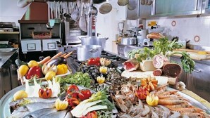 A kitchen with stainless steel appliances, a variety of fresh seafood, and vegetables displayed on the counter. - Hotel Cavalluccio Marino (Gabicce Mare)
