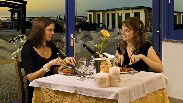 Zwei Frauen essen an einem Tisch mit Blick auf ein Gebäude und ein Gewässer.