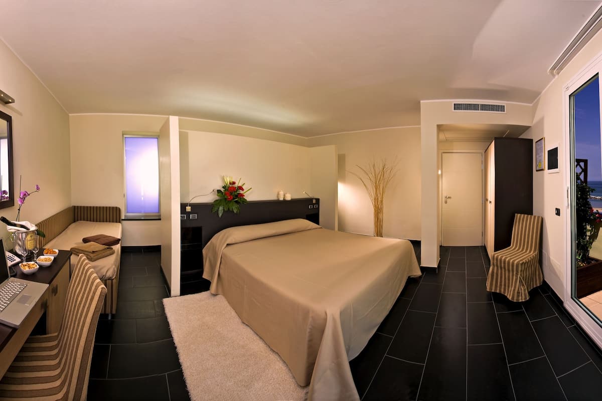 Ein Hotelzimmer mit Bett, Schreibtisch mit Laptop, Stuhl, einem großen Spiegel und Meerblick.