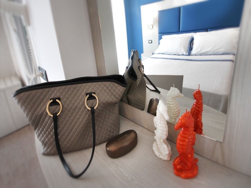 Een bed met een blauw hoofdeinde, een grijs gebogen tas, een zwarte muis en twee decoratieve zeewezens.