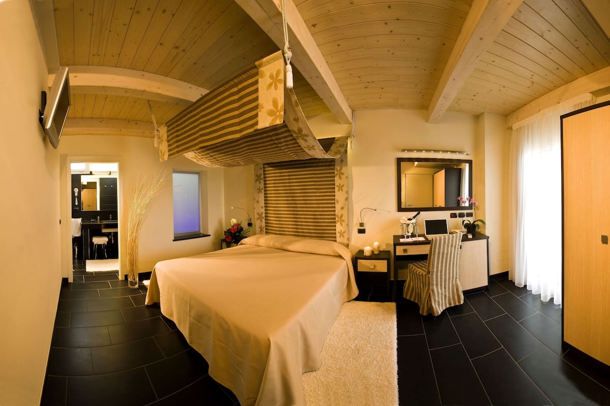 Ein Hotelzimmer mit einem großen Bett, einem Schreibtisch mit Spiegel, einem kleinen Fenster und einem Holzschrank.