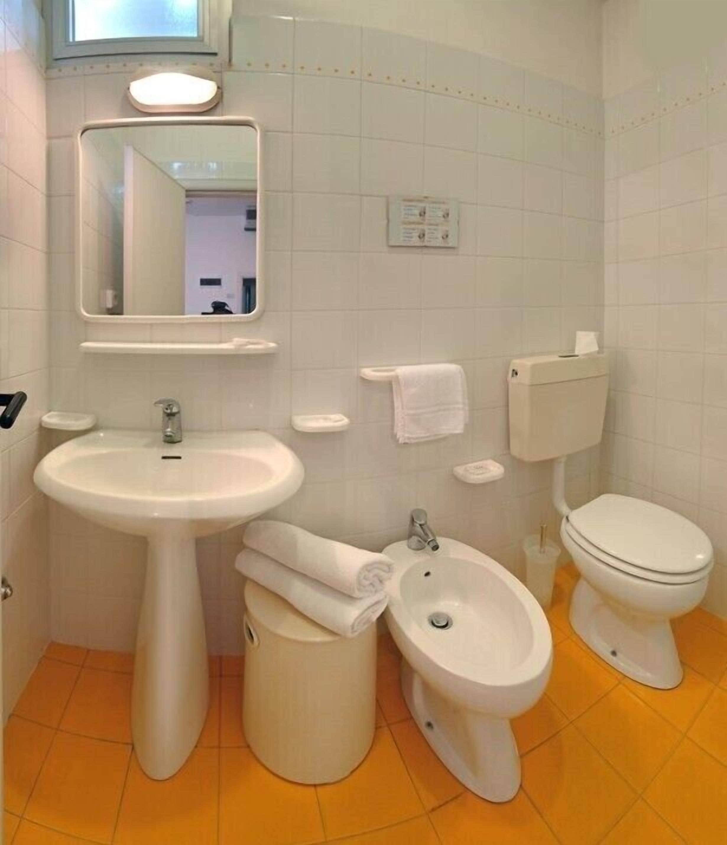 A bathroom with a pedestal sink, a bidet, a toilet, and a mirror.