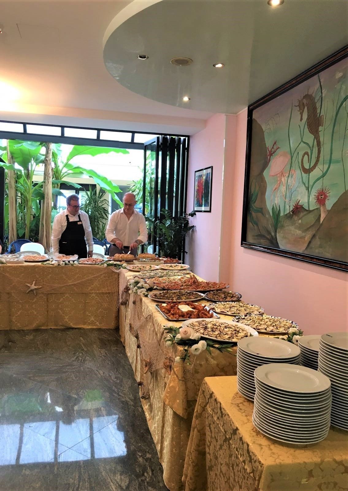 A buffet setup with various dishes, a large painting on the wall, and a ceiling with recessed lighting.